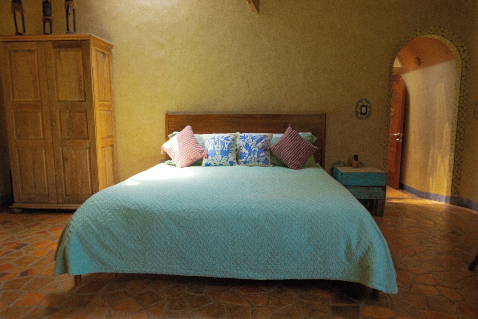 A bedroom with a large bed, a wooden wardrobe, and a tiled floor.