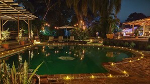 A nighttime pool area with a clear pool, surrounding lounge chairs, and string lights. - EL EQUIMITE HOTEL BOUTIQUE (Coatepec)