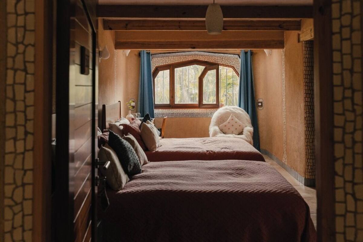 A cozy bedroom with two beds, a window with curtains, and a stone wall.