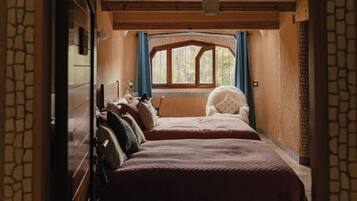 Um quarto aconchegante com duas camas, uma janela com cortinas e uma parede de pedra.