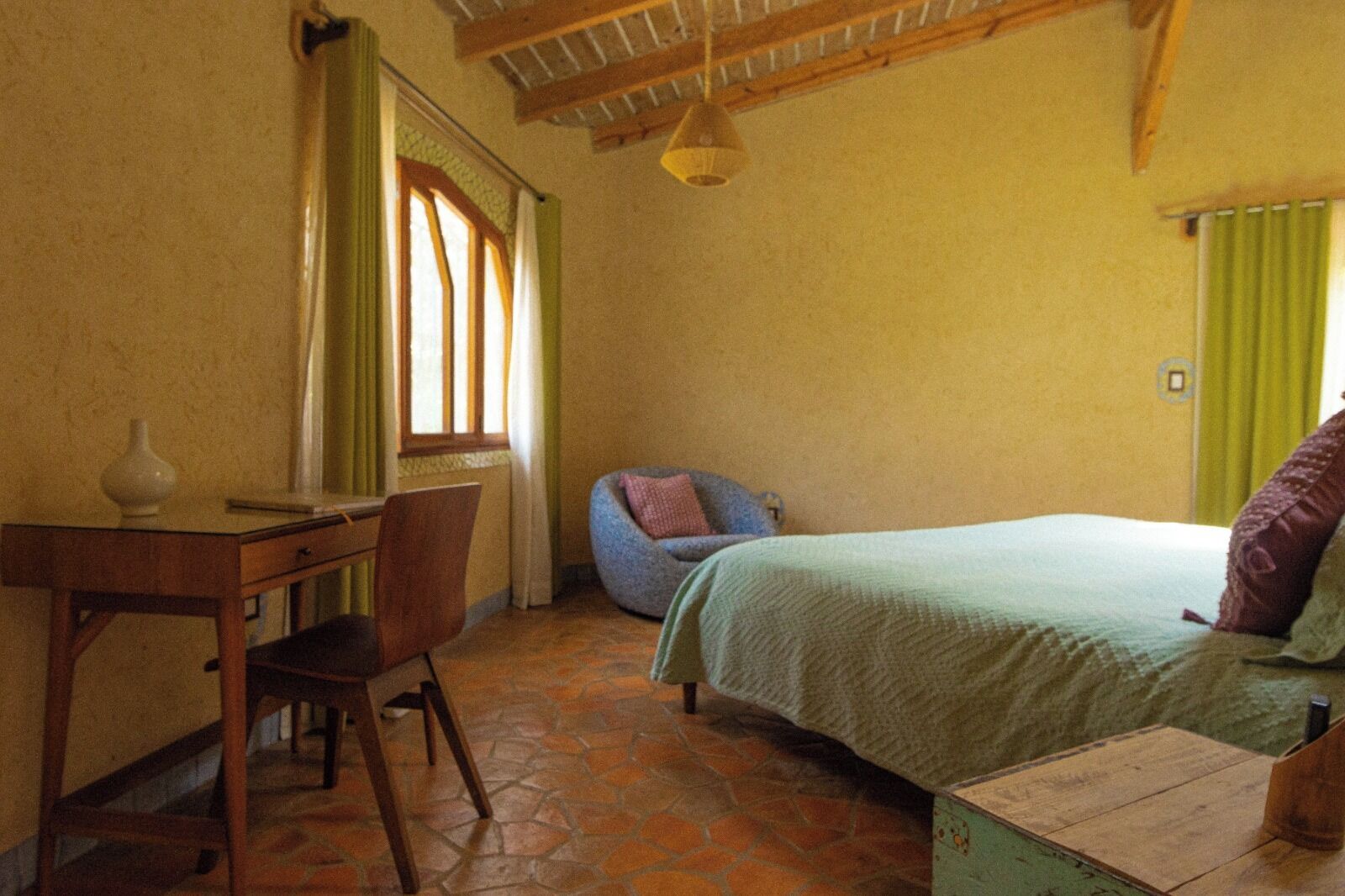 Un dormitorio con cama, una silla, un escritorio y una ventana con cortinas.