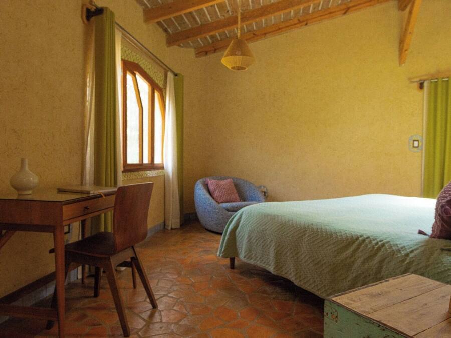 Un dormitorio con cama, una silla, un escritorio y una ventana con cortinas.