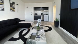 A modern living room with a black sofa, a marble coffee table, and a kitchen in the background.