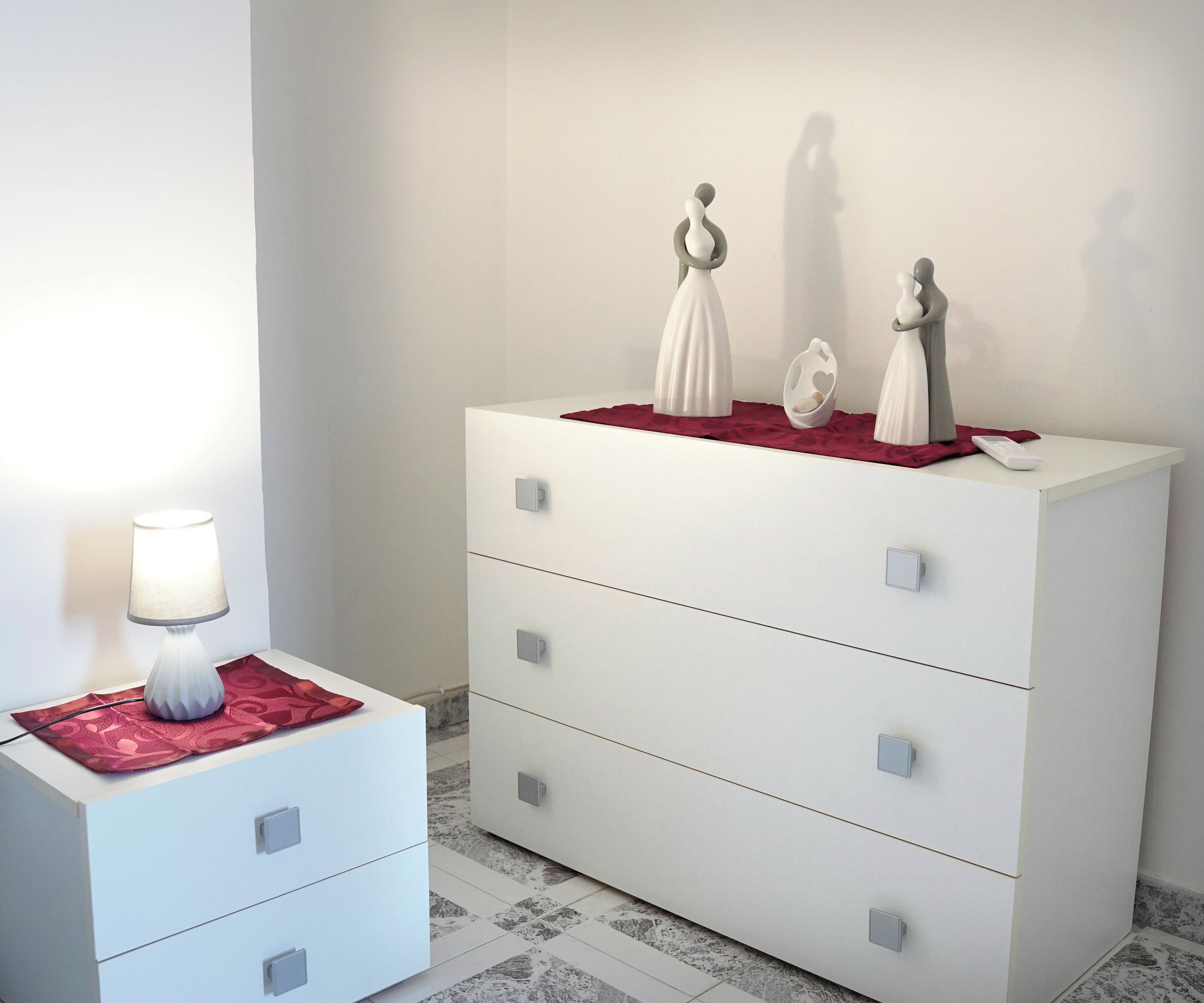 A white dresser with drawers and a lamp on a side table.