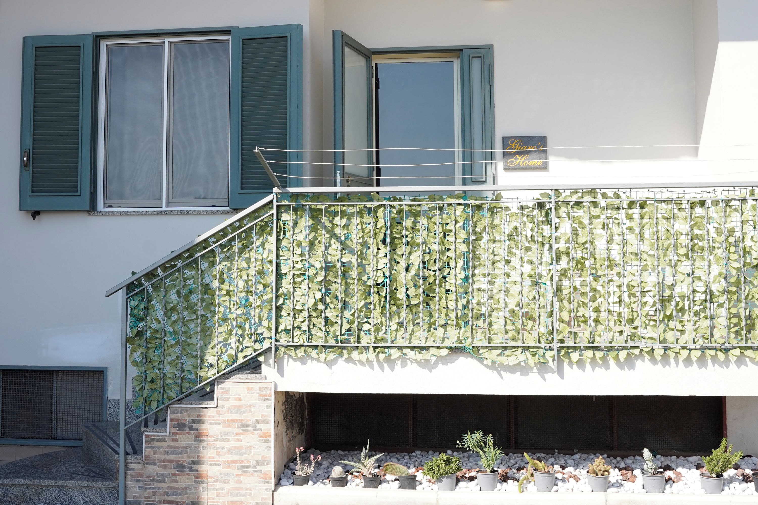 Ein Gebäude mit einer Treppe, einem Balkon mit Kletterpflanzen und Blumentöpfen am Fuß.