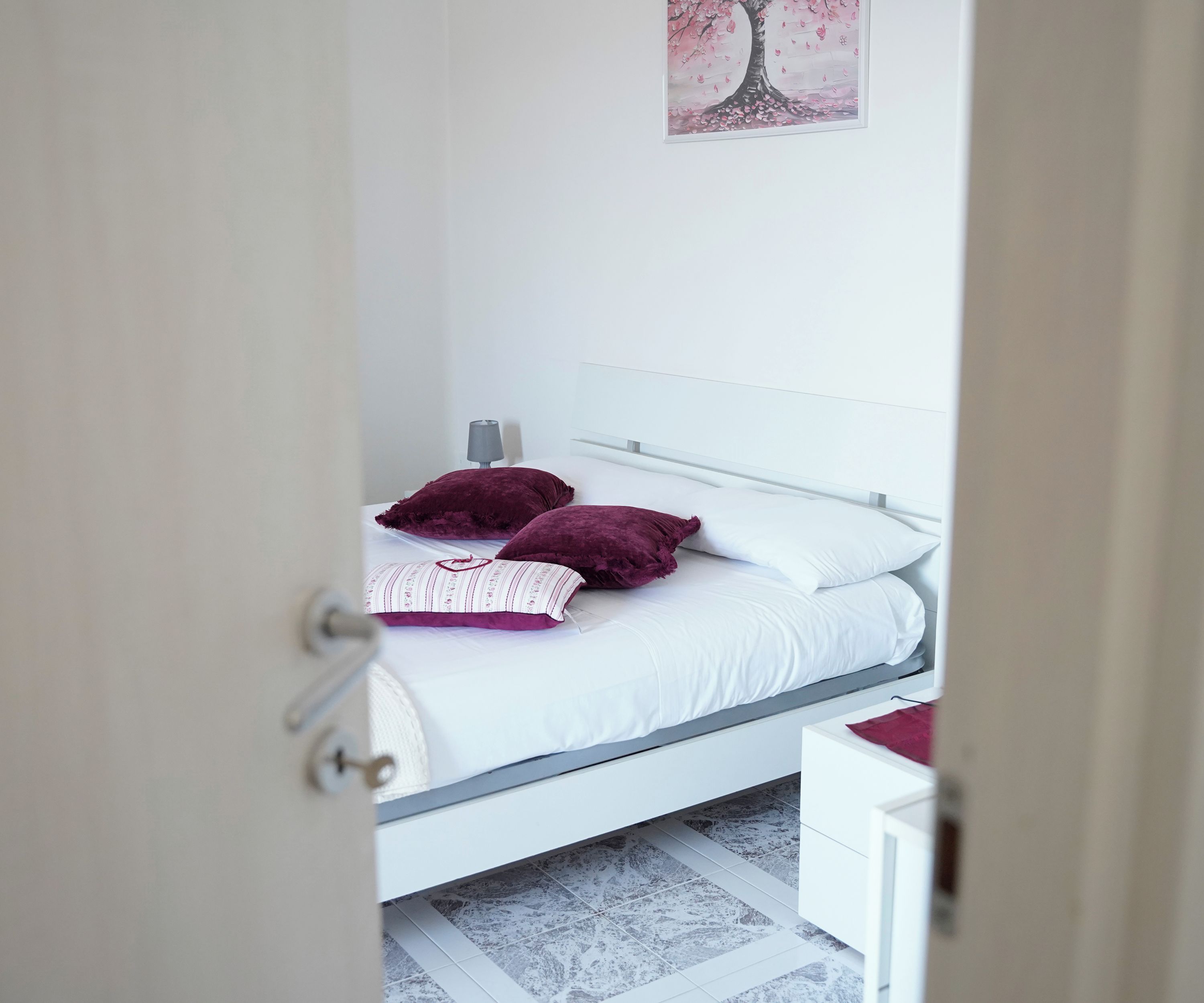 Een slaapkamer met een bed, nachtkastje, lamp en een kunstwerk aan de muur.