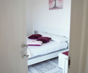 Un dormitorio con cama, mesita de noche, lámpara y una obra de arte en la pared.