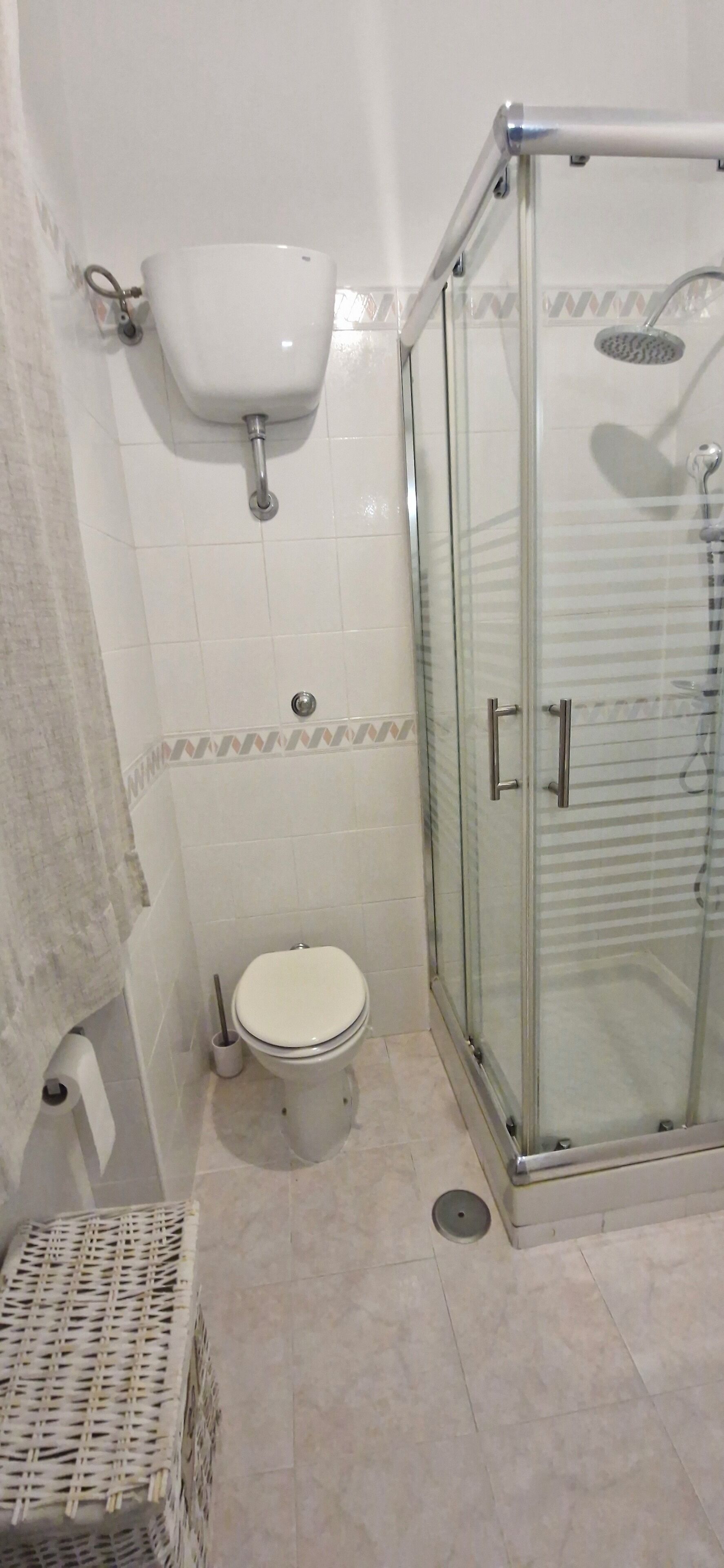 Ein Badezimmer mit Toilette, einer Glaskabine zur Dusche und einem Korbwäscheschrank.