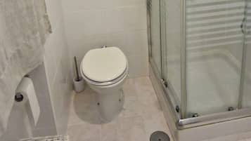 Ein Badezimmer mit Toilette, einer Glaskabine zur Dusche und einem Korbwäscheschrank.