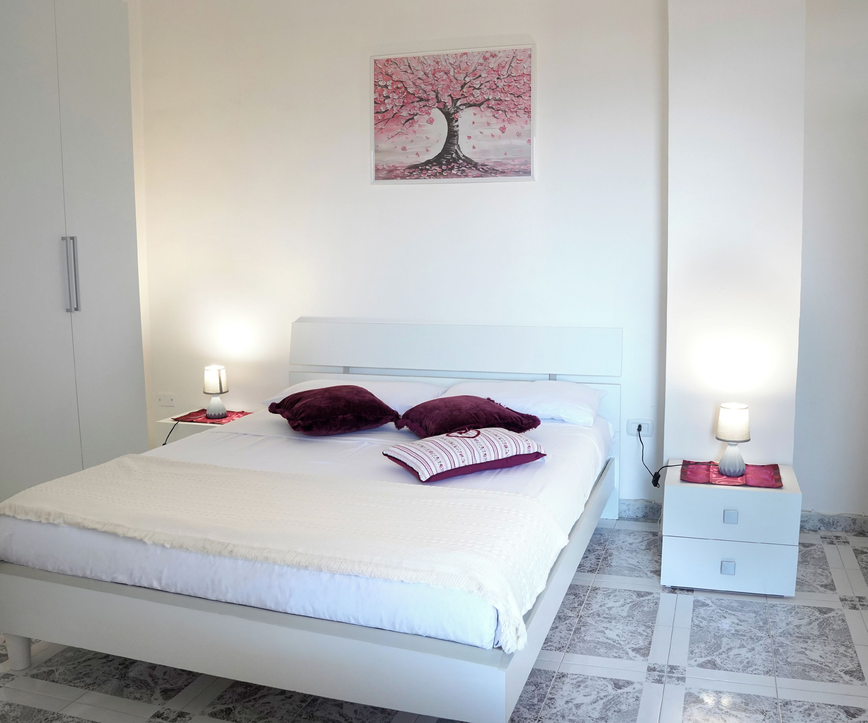 Ein Schlafzimmer mit einem Bett, zwei Nachttischen, einer Nachttischlampe und einem an der Wand hängenden Bild.