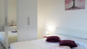 Un dormitorio con cama, almohadas, una lámpara de noche, un espejo y un cuadro en la pared.