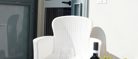 A white wicker chair and table set outside a door with a sign above it.