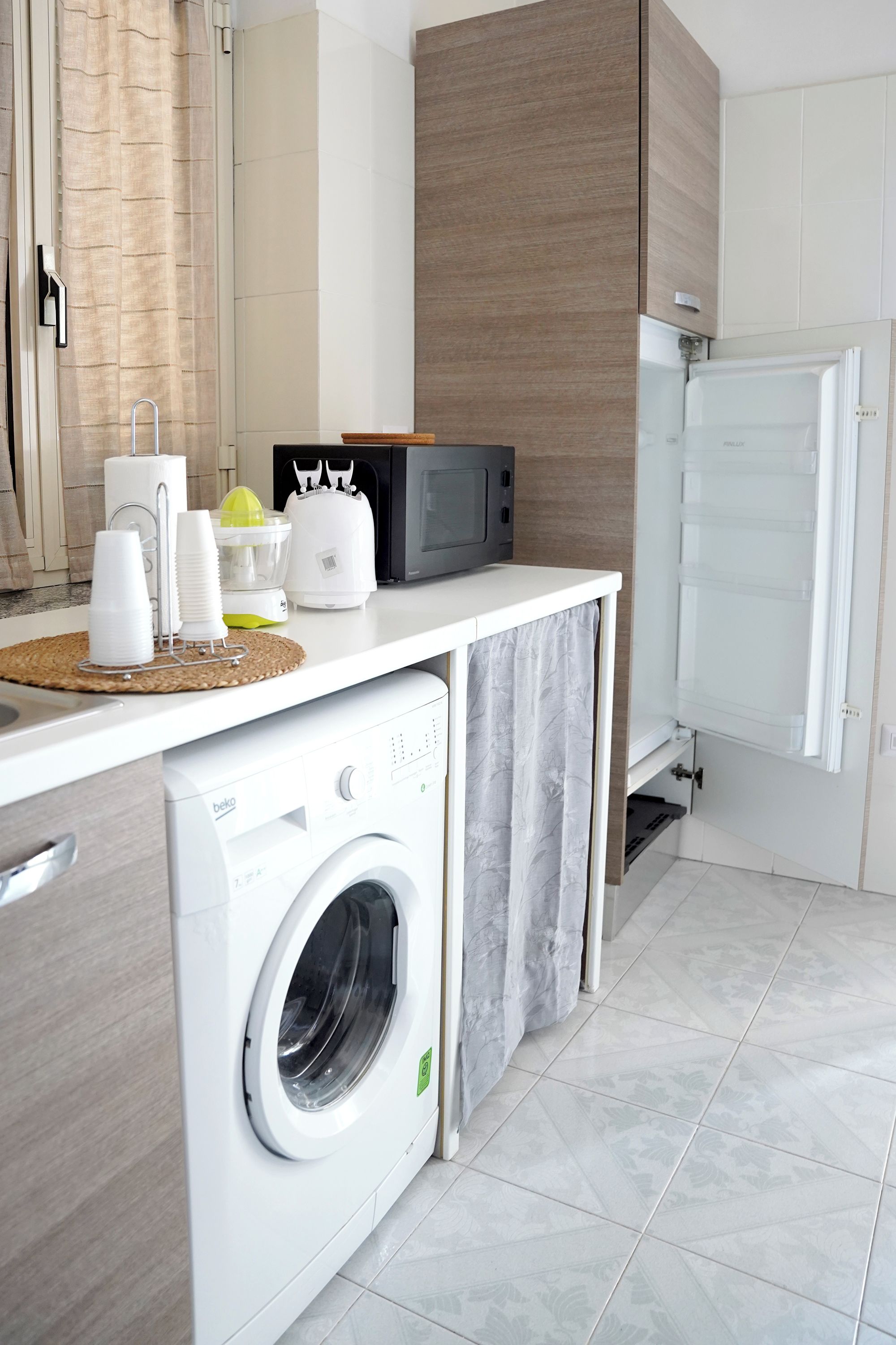 A compact kitchen with a washing machine, microwave, and a small refrigerator.