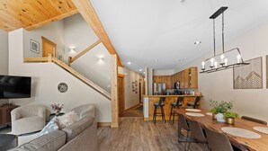 A modern living room with a sofa, a TV, and a staircase leading to a kitchen with wooden cabinets and a dining area with a table and chairs. - St8716-3 (Keystone)