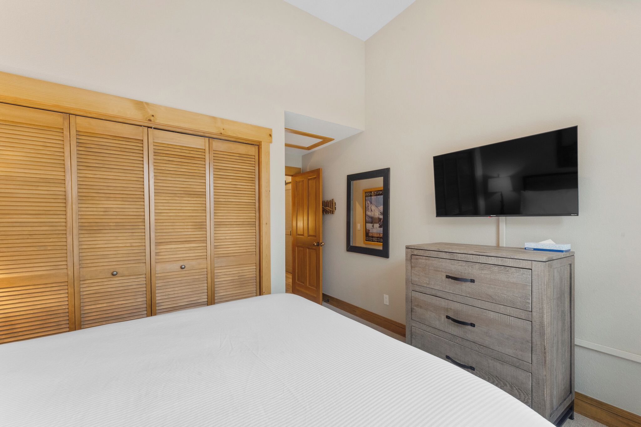 A bedroom with a large bed, wooden closet, a dresser, a television, and a framed picture on the wall.