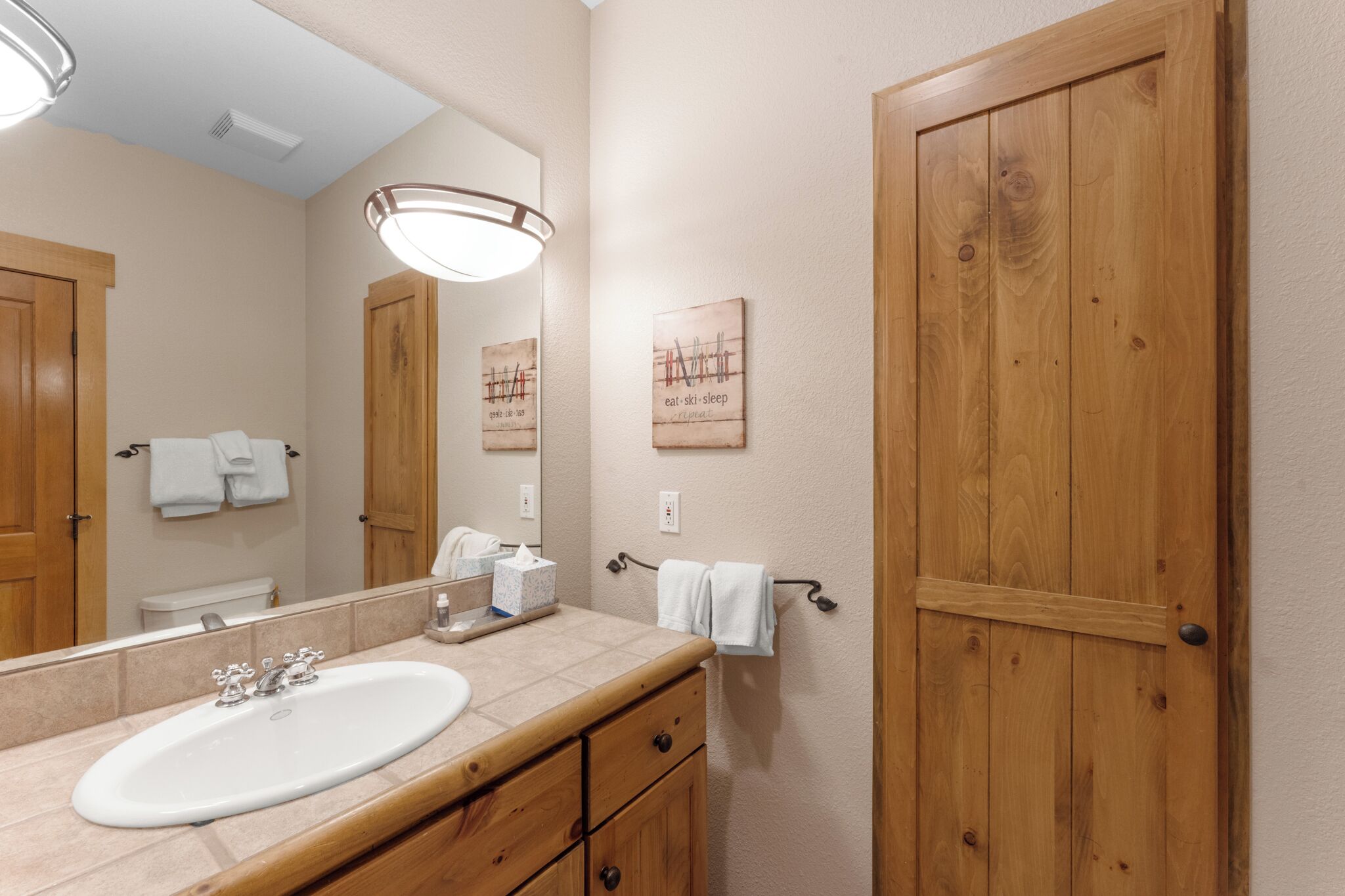 Un baño con lavamanos, espejo, puertas de madera y un perchero para toallas.