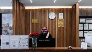 A reception desk with a wooden backdrop, a clock, and informational signs. - Diamond Corners Serviced Apartments (Madinah)