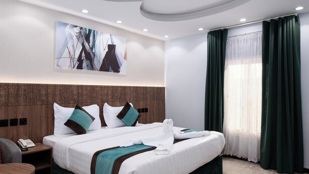 A hotel room with a large bed, a bedside table with a phone, a headboard with a geometric pattern, and a painting on the wall. - Diamond Corners Serviced Apartments (Madinah)