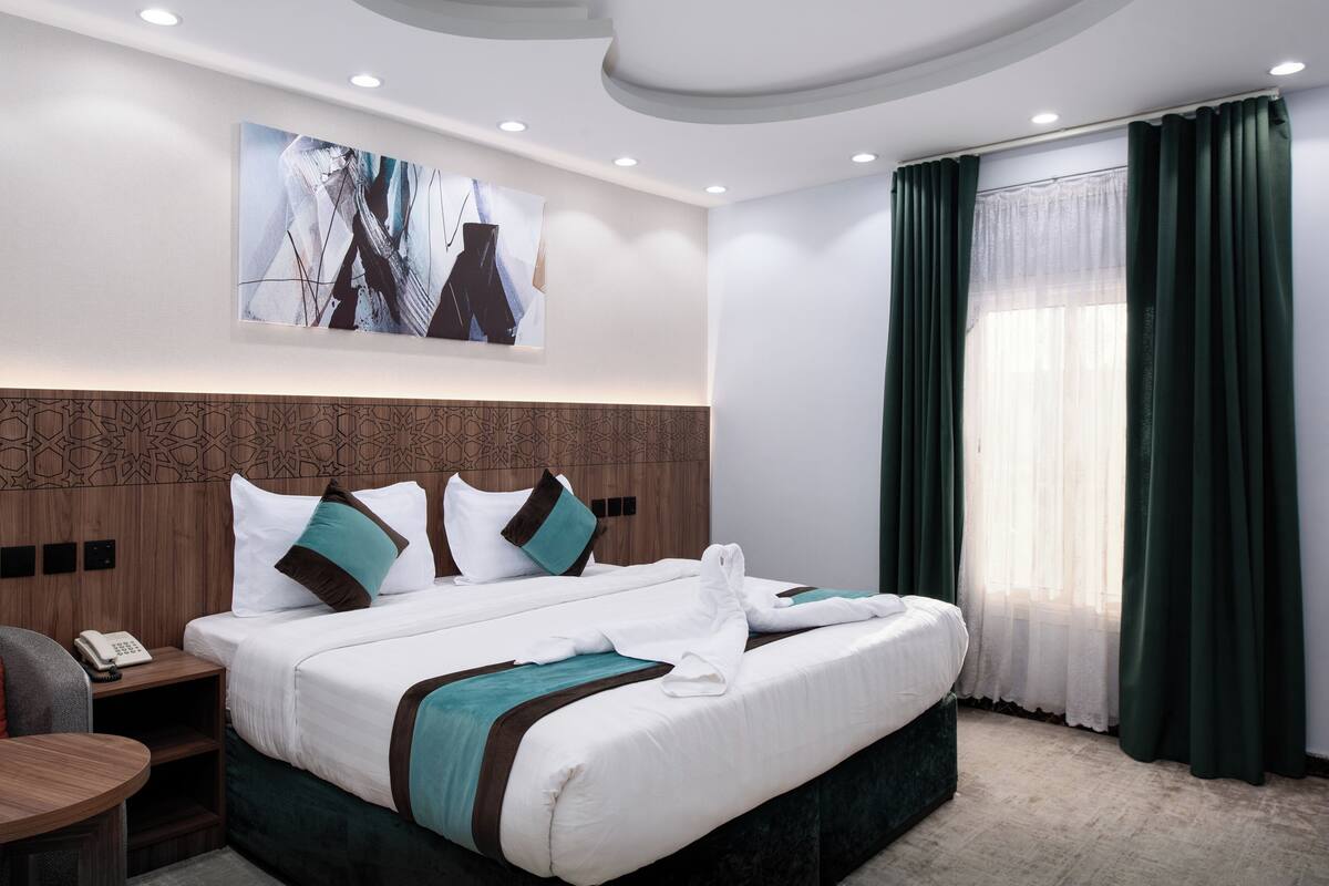 Een hotelkamer met een groot bed, een nachtkastje met telefoon, een hoofdbord met een geometrisch patroon, en een schilderij aan de muur.