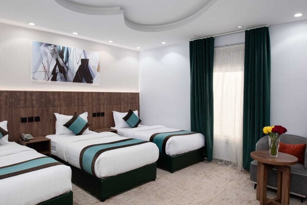 Una habitación de hotel con tres camas, una mesita y una silla.