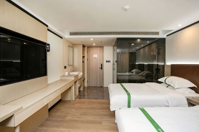 Una habitación de hotel con cama, mesita de noche, televisor y baño con espejo y lavamanos.