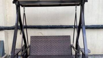 A swing seat with a metal frame and a woven seat cushion, attached to a metal canopy.