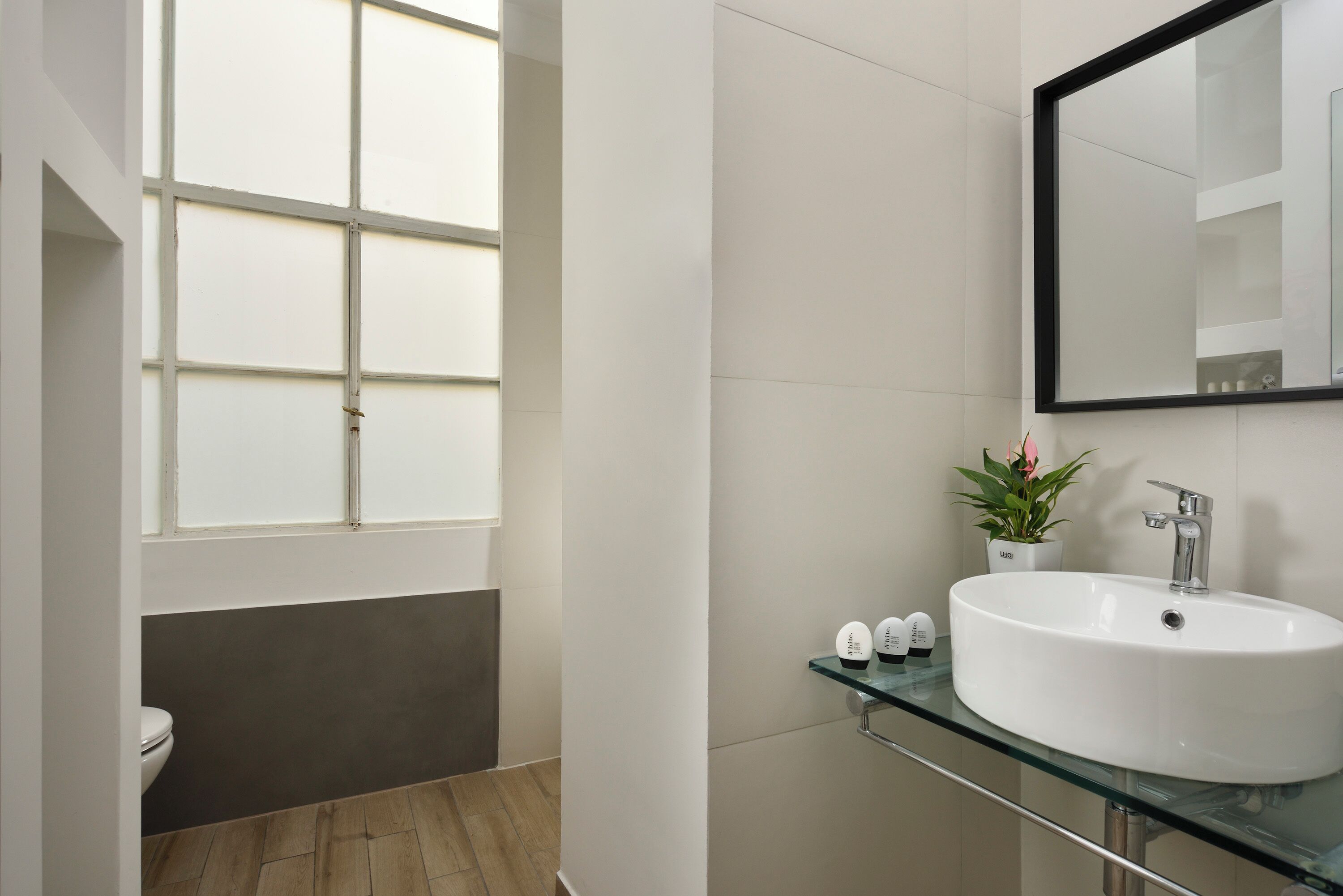Un baño moderno con un ventanal grande, un lavamanos blanco y un estante de vidrio.