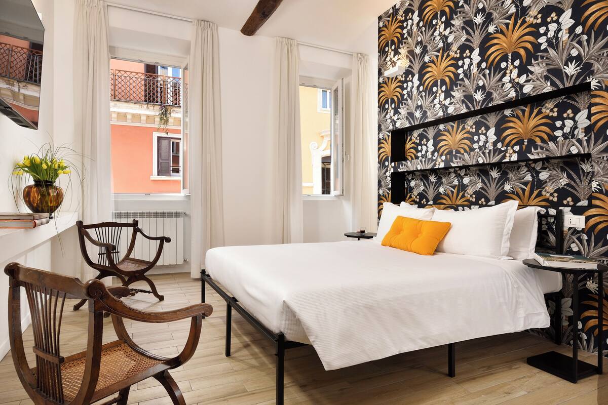 A bedroom with a bed, a chair, a small table, and a wall with a floral pattern.