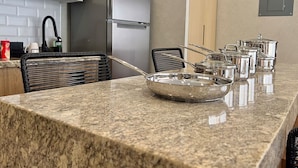 Una cocina con encimeras de granito, electrodomésticos de acero inoxidable y un comedor con una silla negra y un bol metálico.