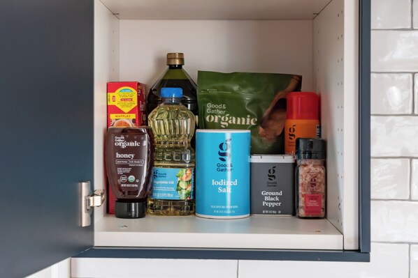 A kitchen shelf with various food items including a box of waffles, a bottle of honey, a can of iodized salt, a bottle of vegetable oil, and a bag of organic coffee.