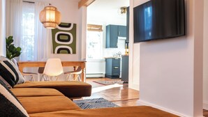 Ein modernes Wohnzimmer mit einer Couch, einem an der Wand befestigten Fernseher und einer Küche im Hintergrund.