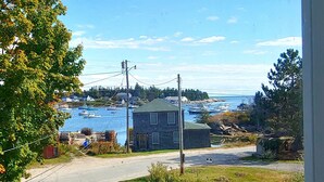 Une vue sur la côte, avec une maison, une zone herbeuse et une étendue d’eau où se trouvent des bateaux.