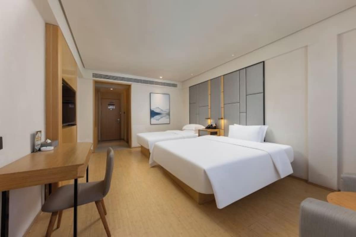 A hotel room with two beds, a desk, and a chair. There is a painting on the wall and a nightstand with a lamp.