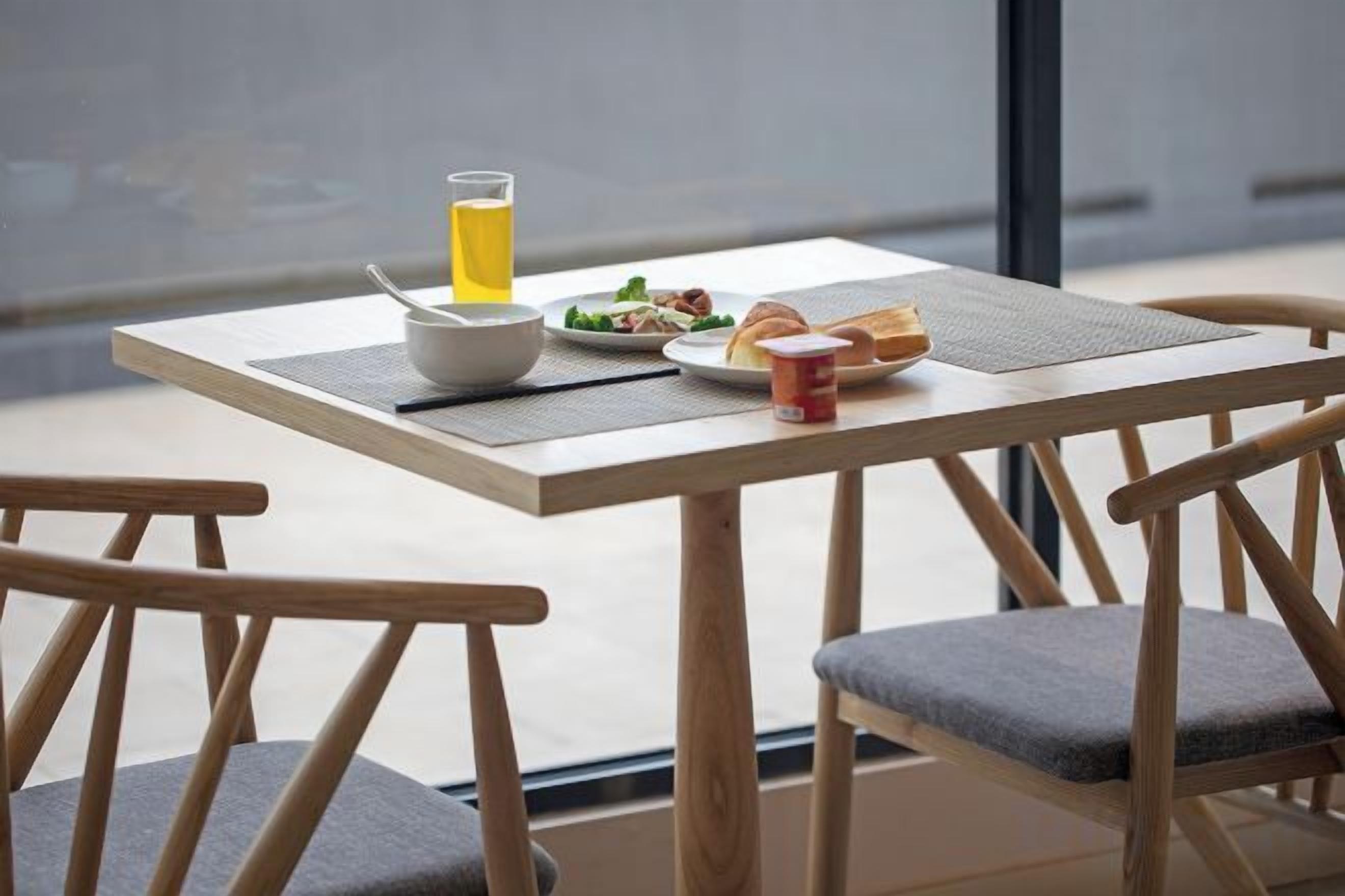 A breakfast table with a bowl, a glass of juice, a plate of food, and a cup.