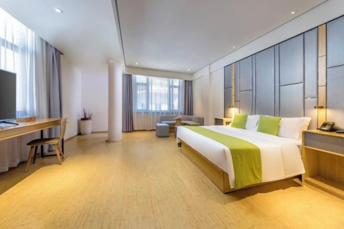 A modern hotel room with a large bed, a desk, a chair, a sofa, and a TV.