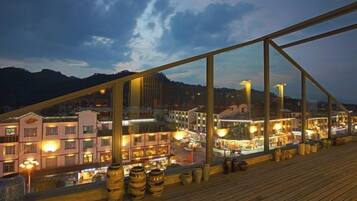 A wooden deck with a view of a town at dusk, featuring buildings and a mountain in the background.