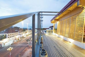 A balcony with a view of a cityscape, a wooden deck, and a building with a modern facade. - Wuyishan Mushi Time Hotel (Impression Dahongpao Store) (Wuyishan)