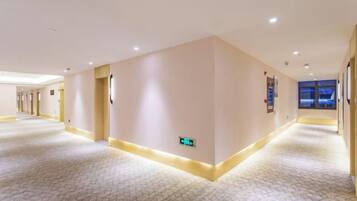 Een hotelgang met een patroon vloer, een lichtgekleurde muur en een deur links.
