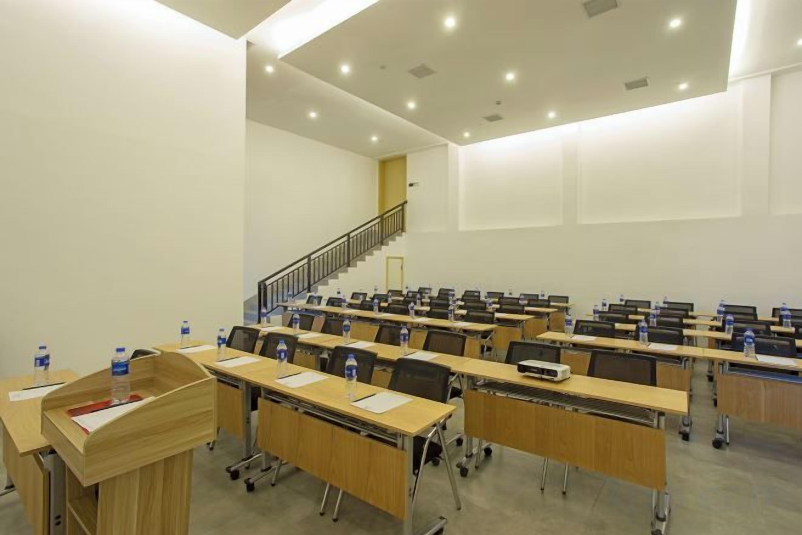 A conference room with rows of tables and chairs, a podium, and a staircase leading to an upper level.