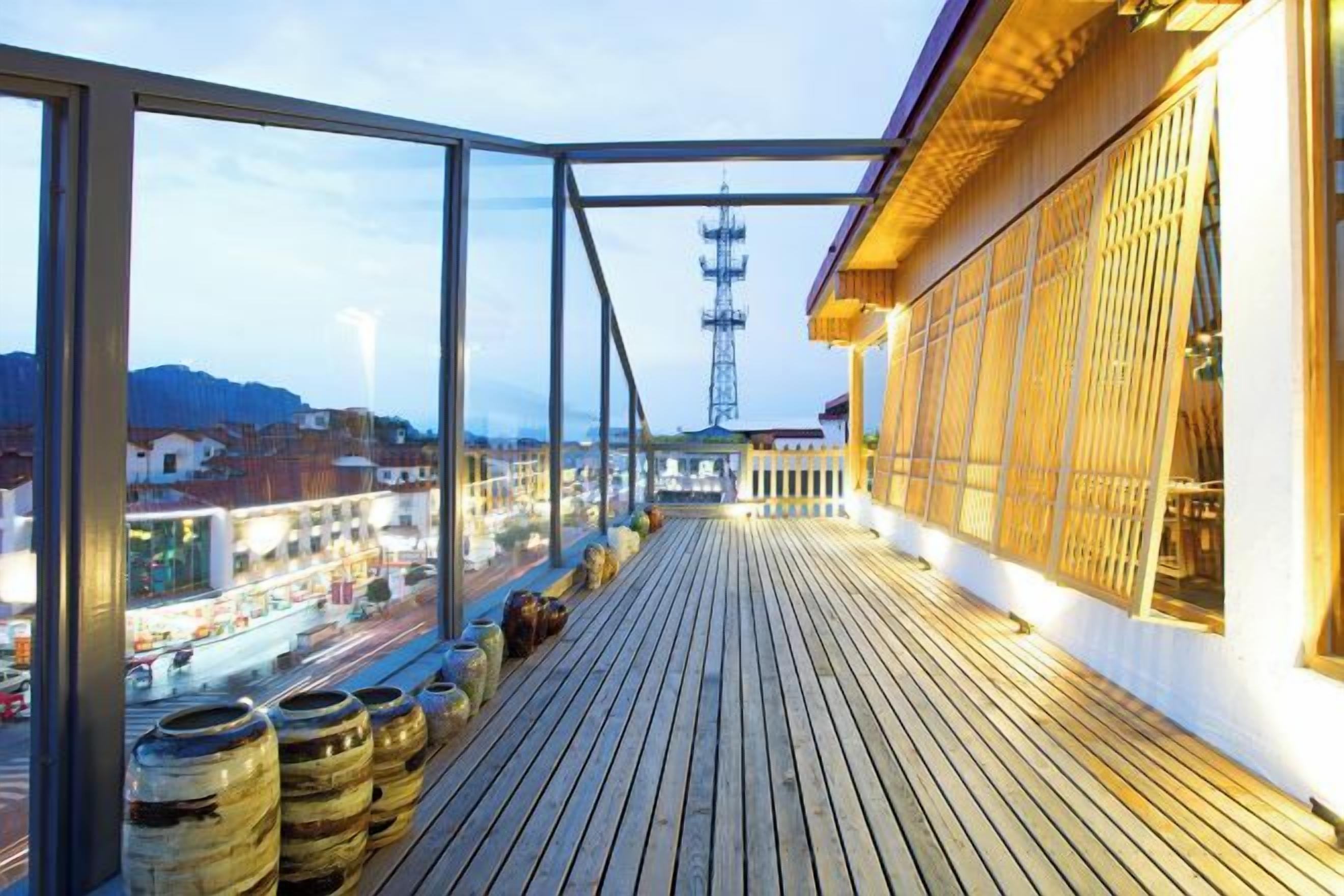 A balcony with a view of a cityscape, wooden flooring, and large windows.