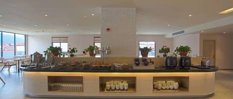 A modern hotel lobby with a central counter, seating area, and potted plants.
