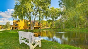 Une vue sur le lac, avec un banc, un bâtiment jaune et une végétation luxuriante tout autour.