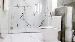 Un baño con inodoro, zona de ducha y paredes de mármol.