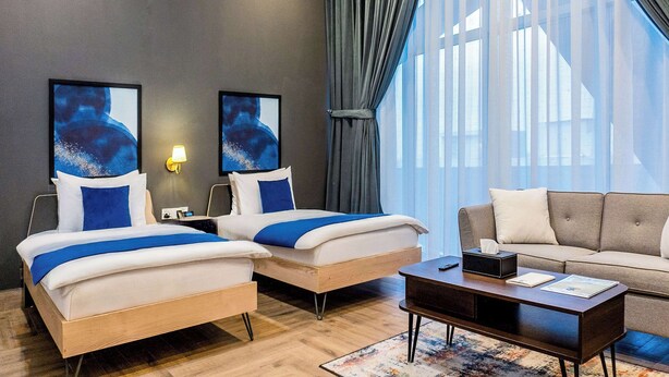 Habitación de hotel con dos camas, un sofá, una mesa de centro y obras de arte en las paredes.