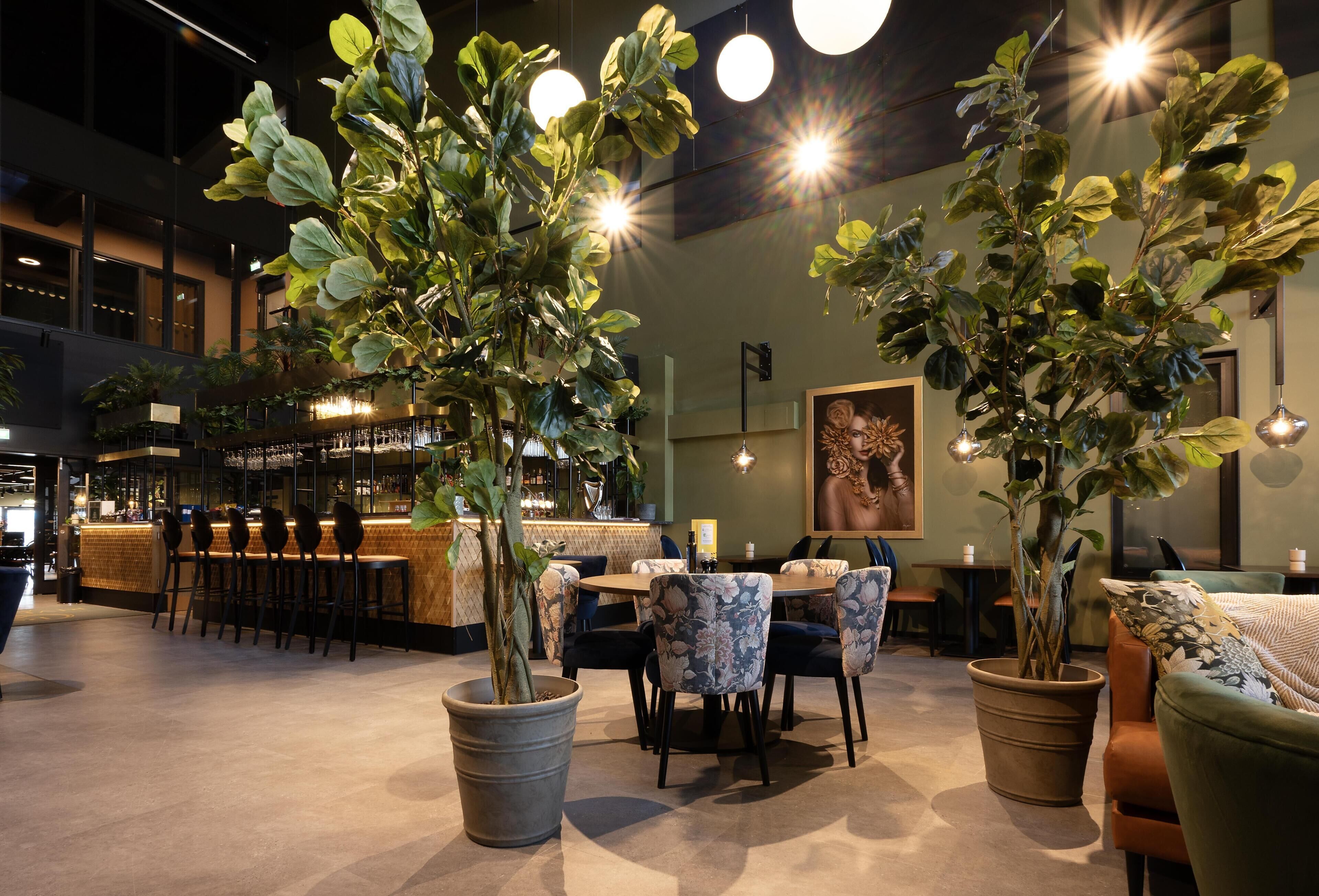 A modern indoor space with a bar area, seating, and potted plants.