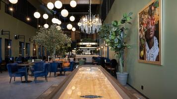 Un interior moderno con una larga mesa de madera, sillas azules, luces colgantes y una zona de bar.