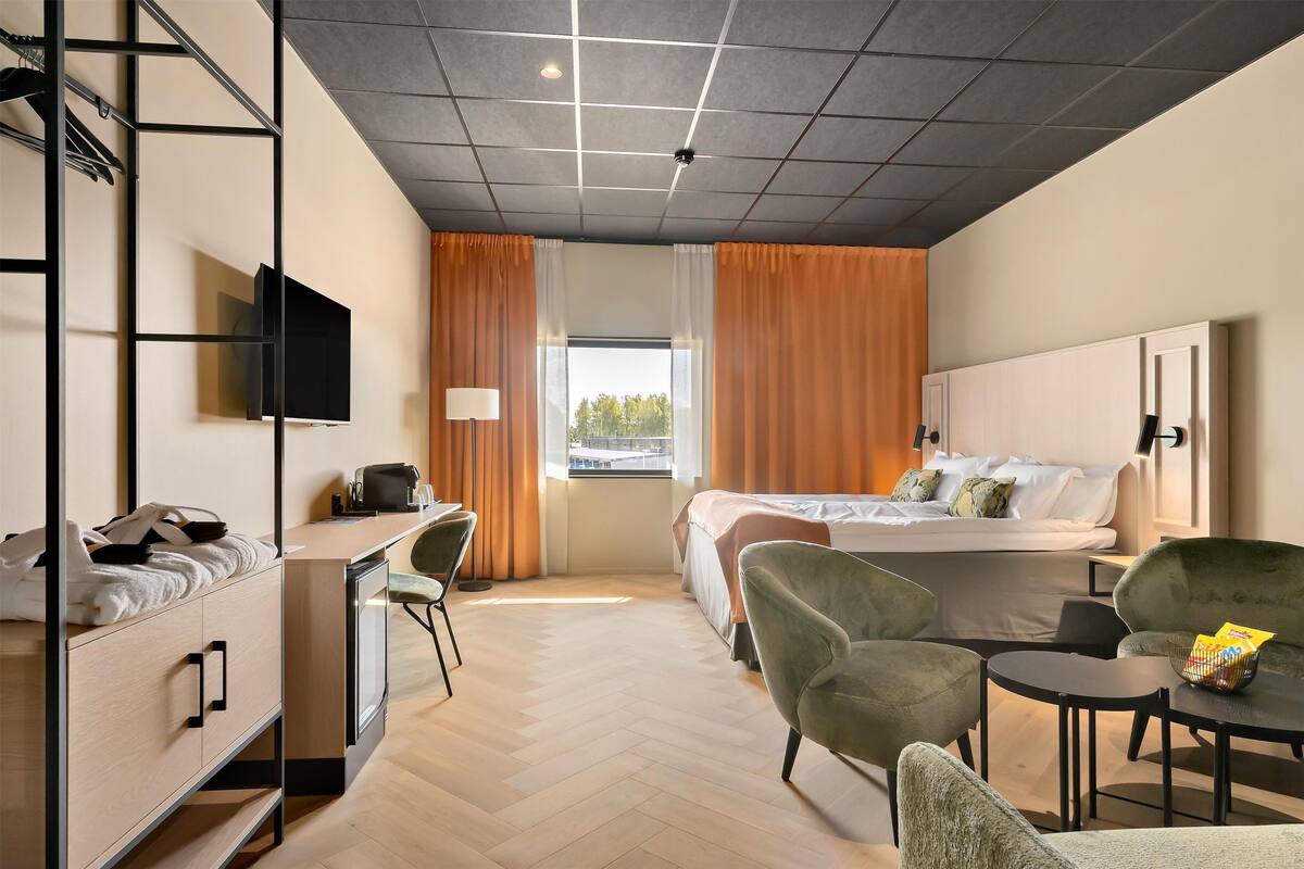 A hotel room with a bed, desk, chair, and a small table with snacks.