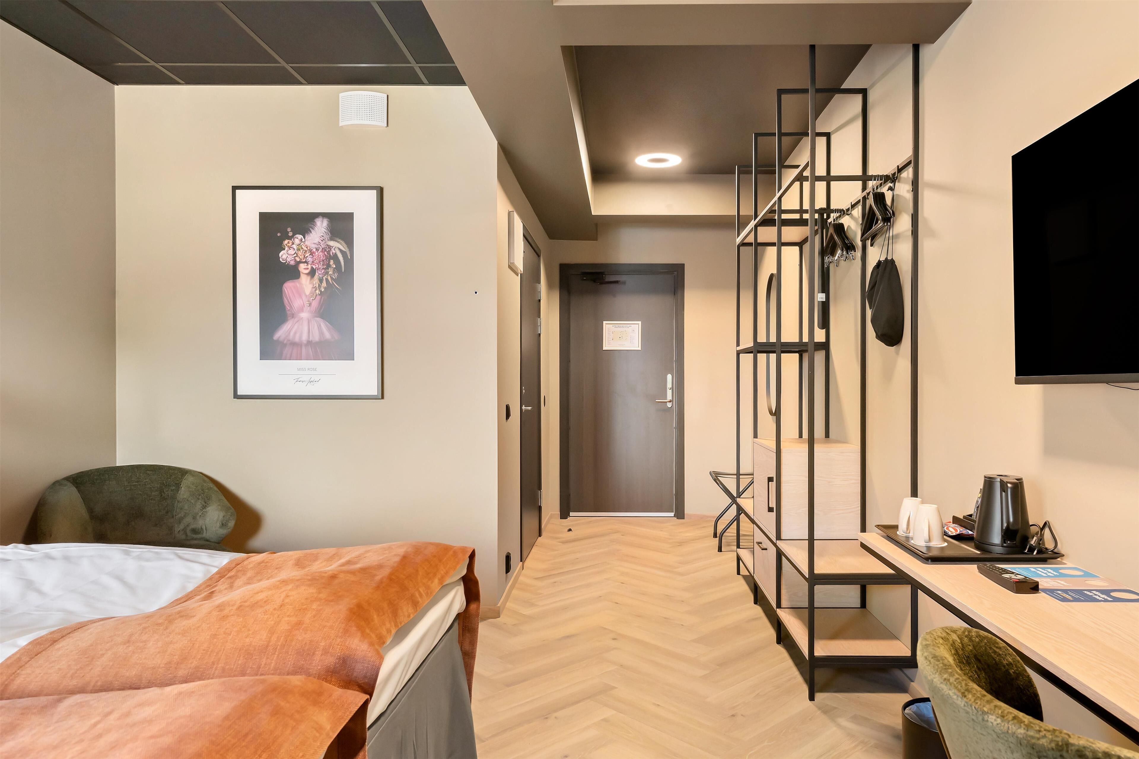 Habitación de hotel con una cama, un escritorio con una silla, un televisor y un cuadro en la pared.