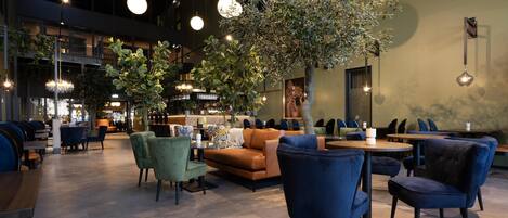 Un espacio interior amplio con diversas opciones de asientos, incluyendo sofás y sillones, y un árbol grande en el centro.