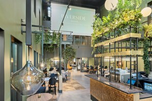 Un intérieur moderne avec un espace bar, des sièges et un grand écran diffusant des images de « RIVERSIDE AVESTA ».